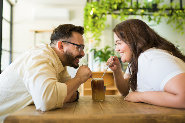 Ein verliebtes Paar - Ein Mann und eine mollige Frau - sitzen in einem Cafe trinkt zusammen und trinken zusammen mit Strohhalmen ein Getränk